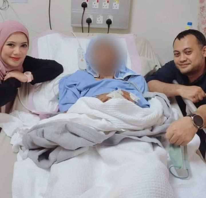 Din di katil hospital (wajah dikaburkan), ditemani dua orang yang tersenyum di sisi katil